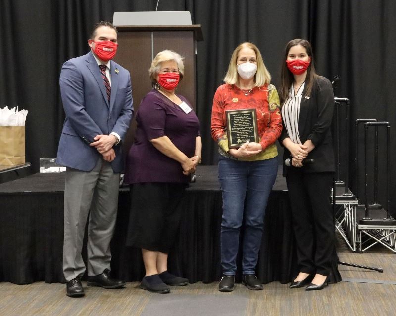 Woman holding plaque poses with three other people.