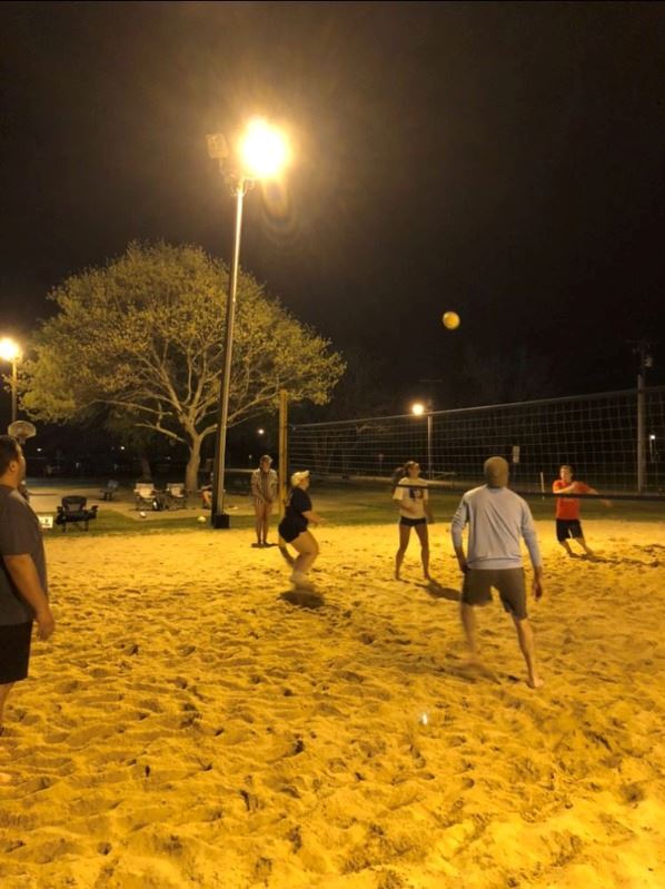 People play sand volleyball in the park at night under a street lamp.