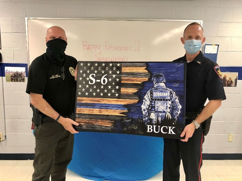 2 police officers hold a canvas print with a thin blue line flag, the name Buck and a uniformed man