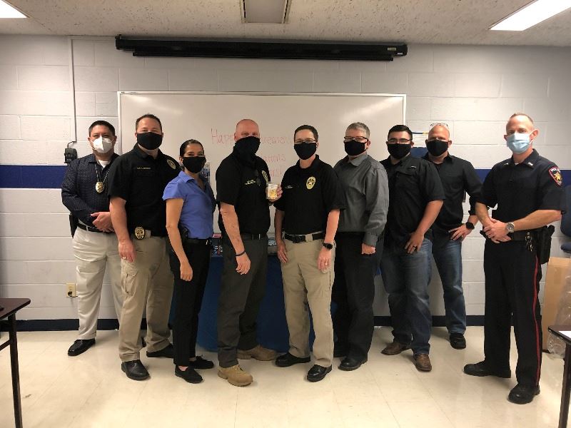 Several uniformed police officers stand together. A man in the middle holds a metal police badge.