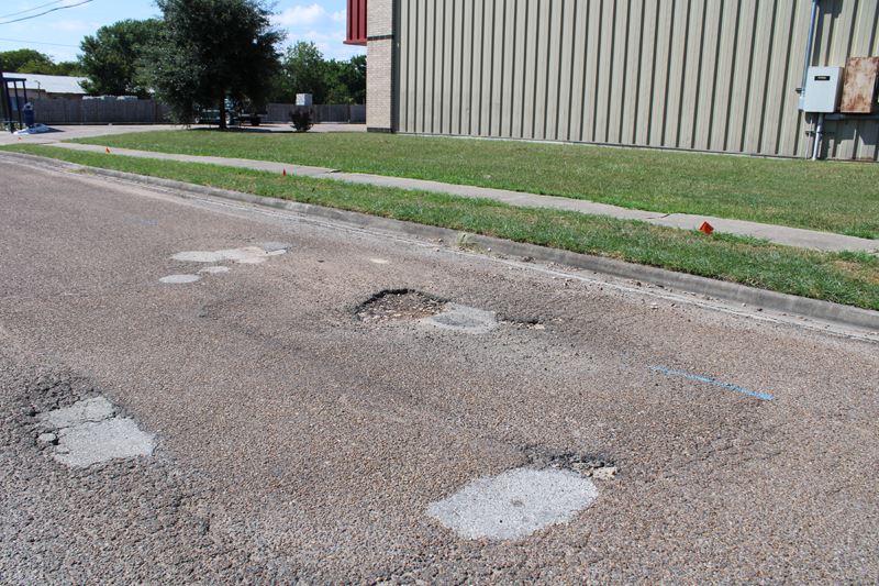 Street with potholes, cracks and discoloration near Salvation Army warehouse