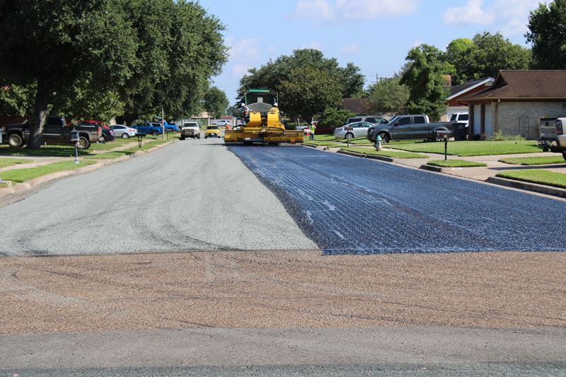 A machine applies a rocky overcoat to a layer of tar on a residential road.