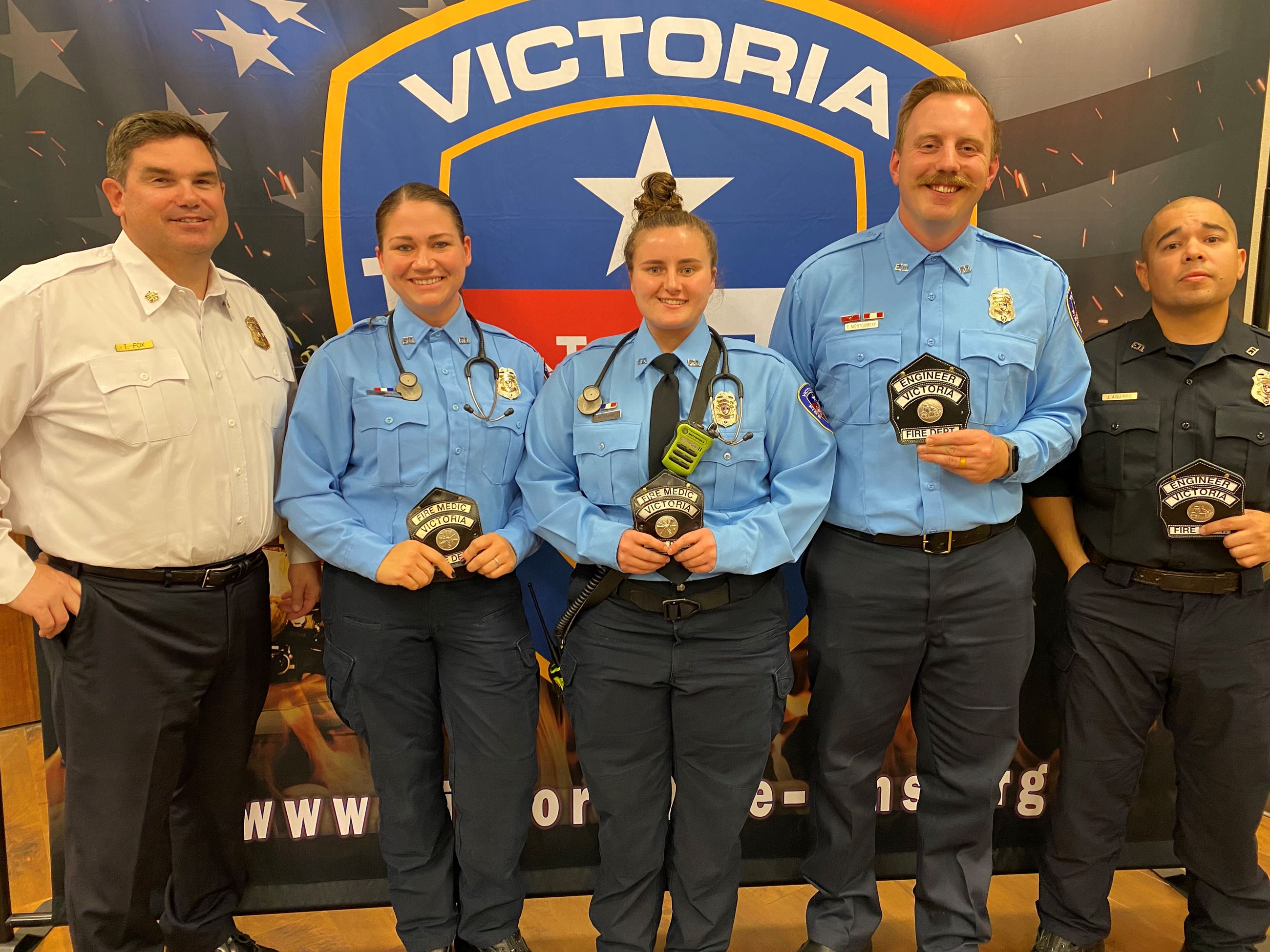 Five people in firefighter dress clothes. 4 hold small black patches. Of those, 2 wear stethoscopes.