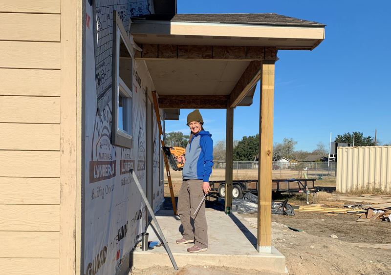 Woman stands on the porch of an unfinished home holding a power drill